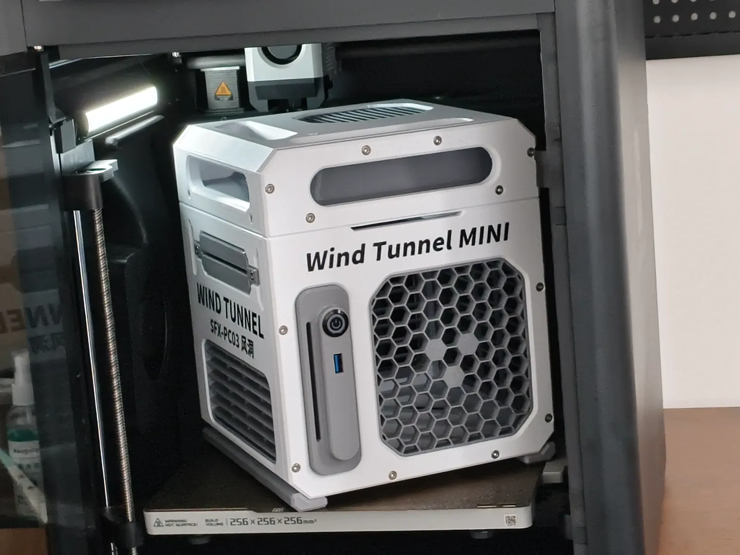 3D-printed white mini-ITX PC case with a hexagonal mesh front fan grille, resting on a print bed